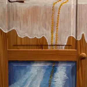 Gallery installation featuring a wooden architectural frame with blue painted canvas panel below and gold rope elements suspended above.
