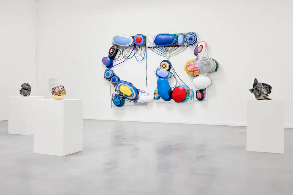 Vibrant mixed-media wall installation with colorful balls, geometric shapes, and suspended elements in blue, red, and purple tones.