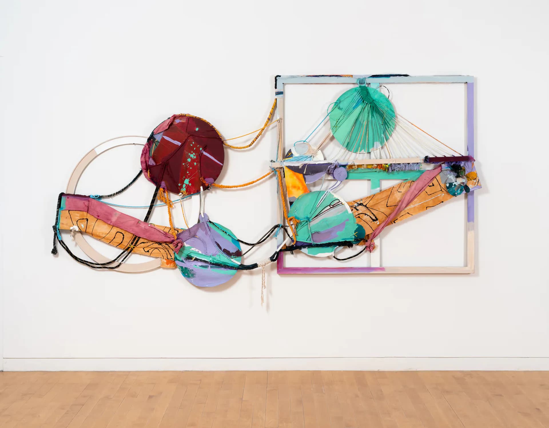 Abstract mixed-media sculpture combining transparent geometric forms, colorful ribbons, and fabric elements in greens, oranges, and reds.