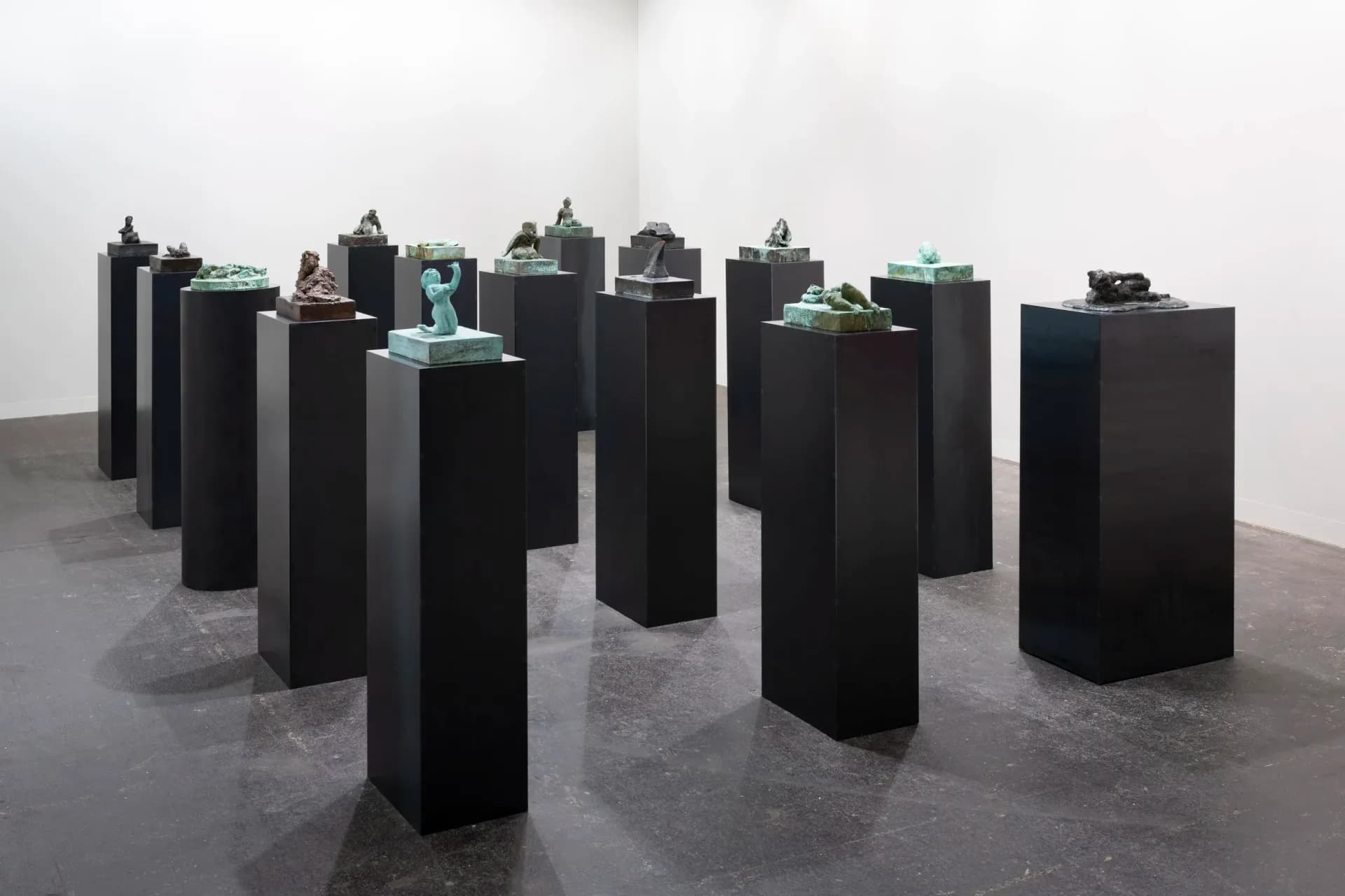 Installation view of black rectangular pedestals with green sculptural objects on top displayed in a white gallery space.