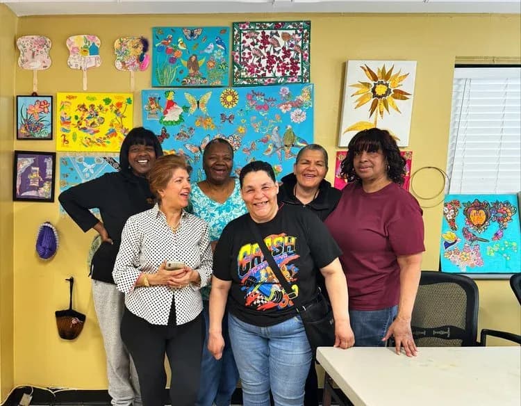 Five people posing together in a bright yellow room with colorful artwork on walls, likely a Carter Burden Center community space.