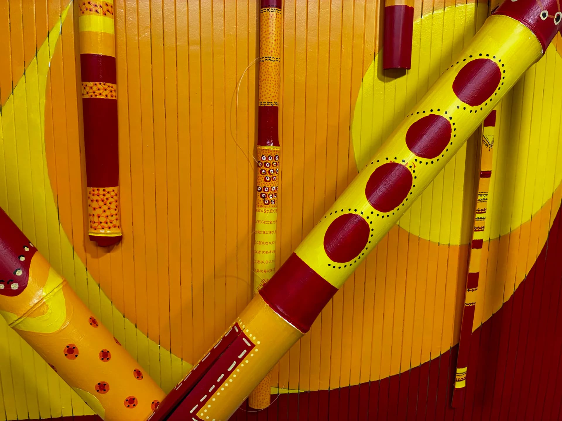 Abstract composition of yellow and burgundy striped forms with geometric patterns, dots, and linear details suggesting musical instruments or architectural elements.