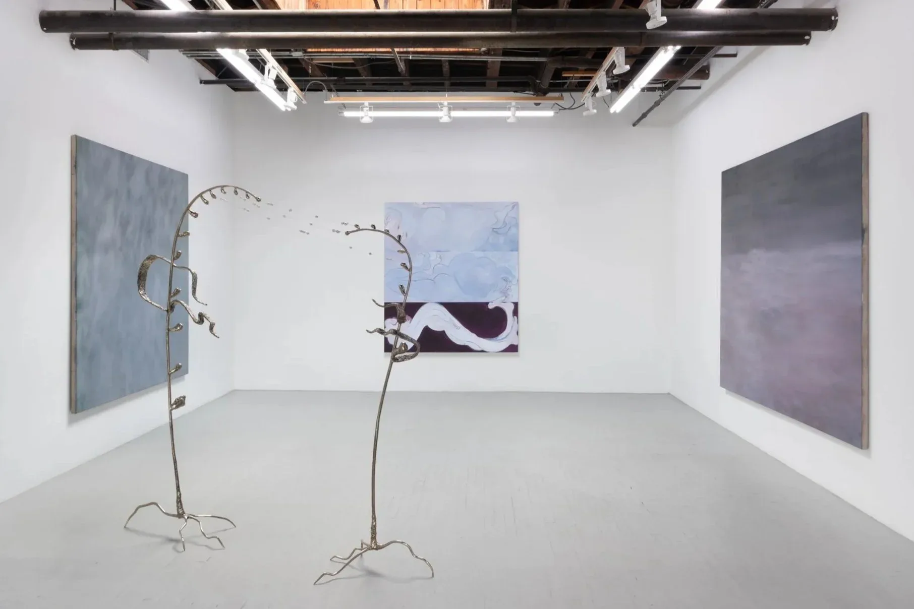 Gallery installation with two metal wire plant-form sculptures with hanging elements and three blue-toned abstract paintings on white walls.