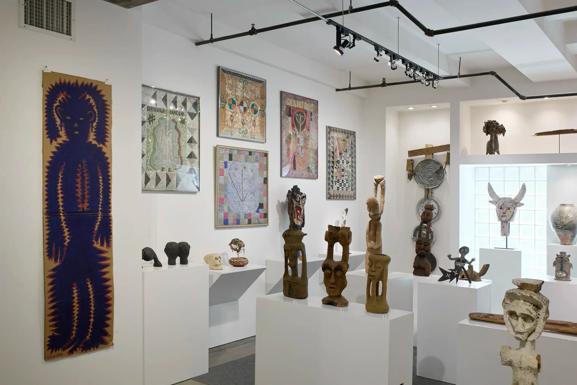 Gallery space at Cavin-Morris Gallery featuring framed artwork on walls, wooden sculptures on pedestals, and display cases with three-dimensional pieces.