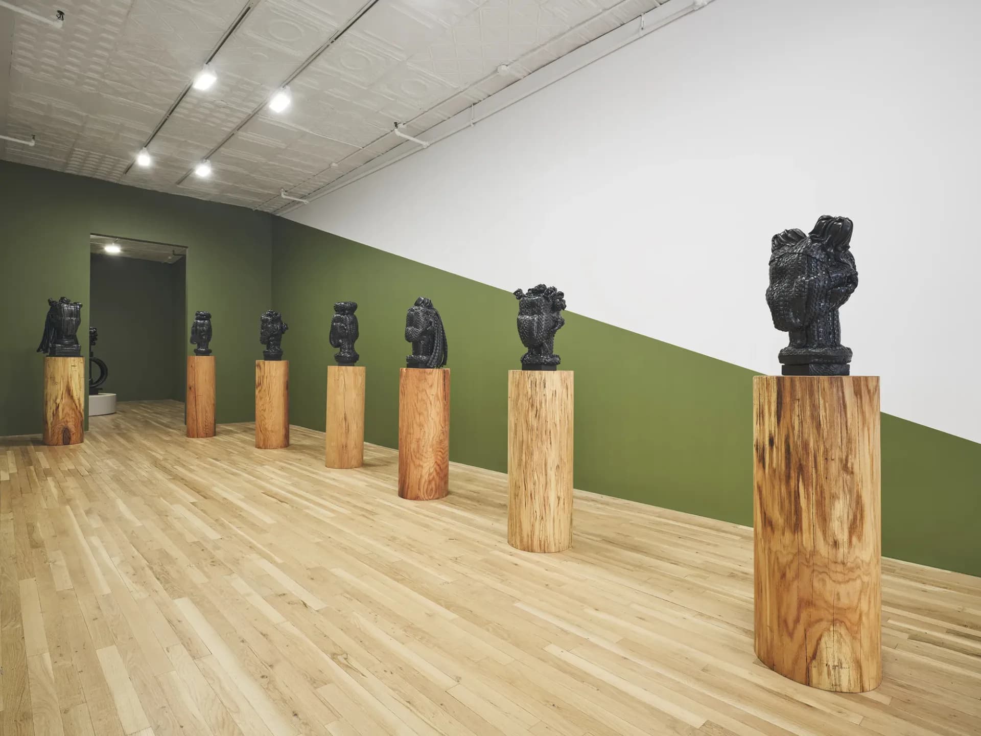 Gallery space with green accent wall displaying black sculptural busts mounted on wooden pedestals.