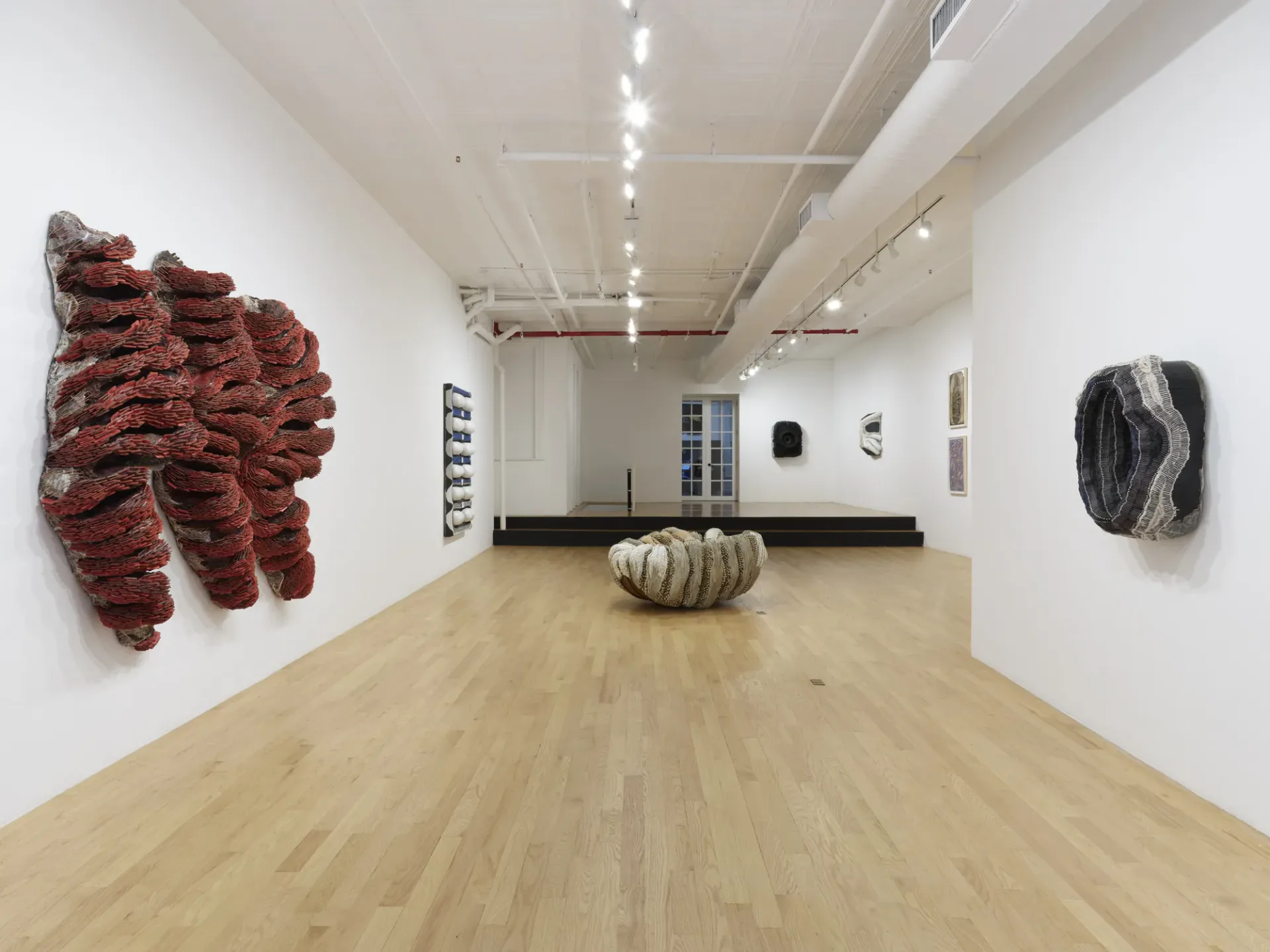CHART gallery interior with wooden flooring, white walls, track lighting, and various mixed-media artworks including red textile and woven sculpture.