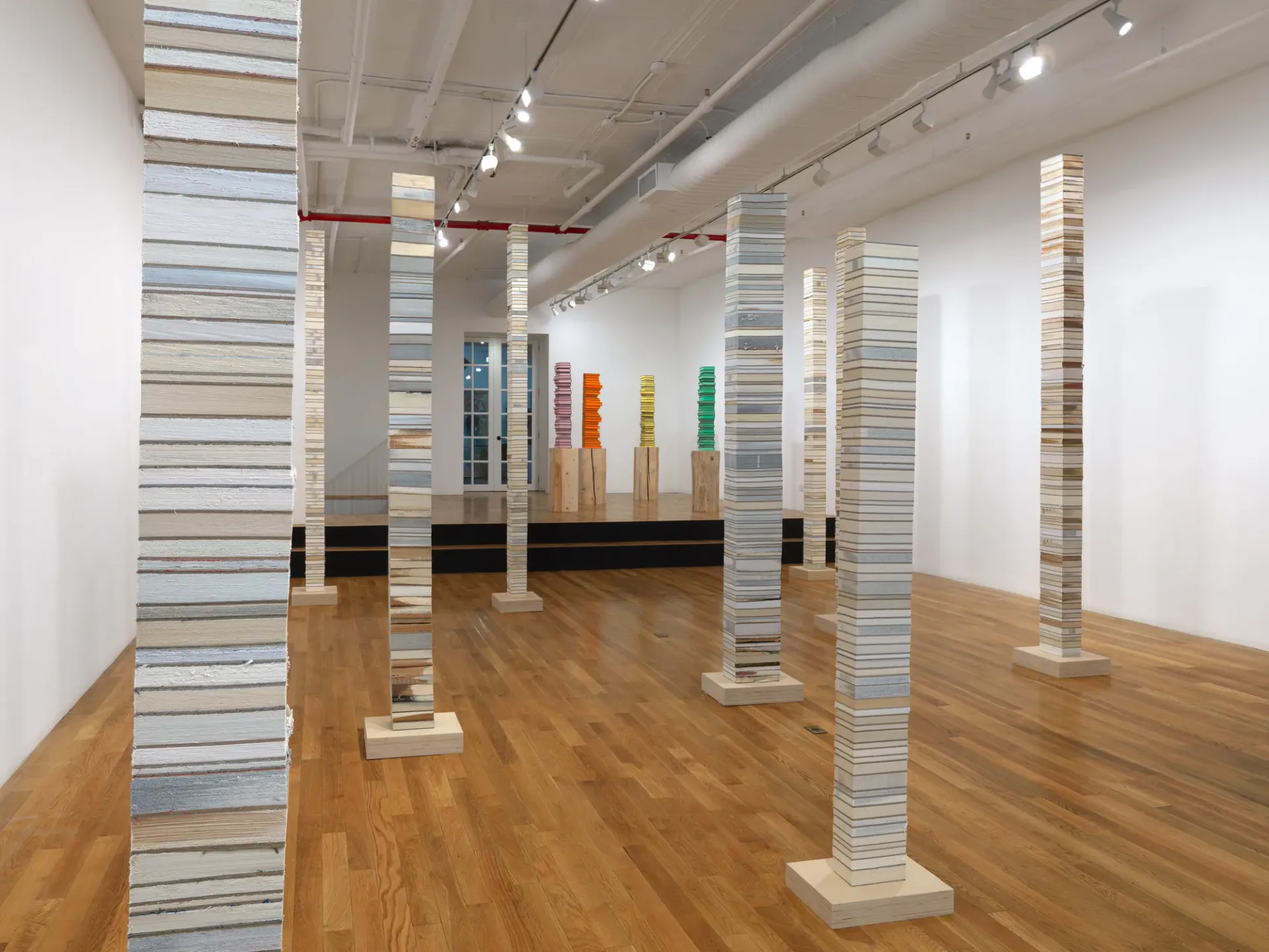 CHART gallery interior with tall columns wrapped in striped paper, wooden floors, track lighting, and white walls creating immersive installation space.
