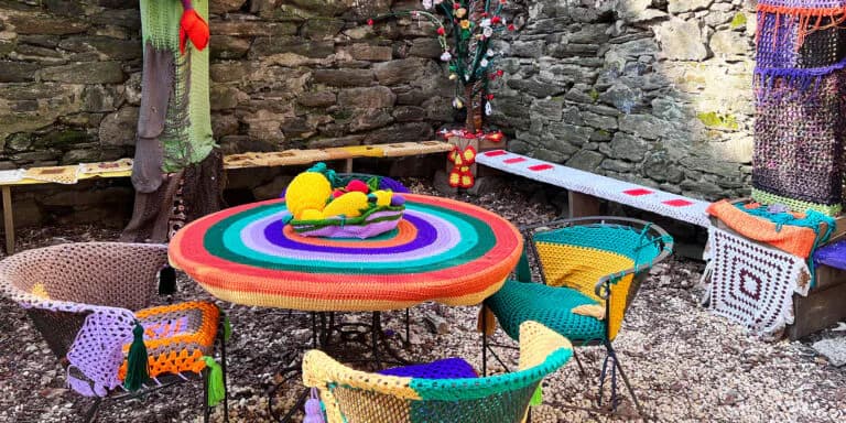 Children's Art Carnival outdoor space featuring colorful woven and crocheted installations including a large red and rainbow spiral centerpiece with decorated chairs.