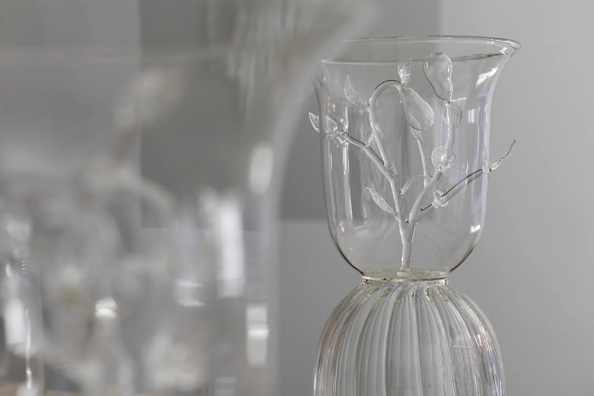 Clear glass vessel with etched botanical branch design and ribbed base, photographed against neutral background with soft shadows.