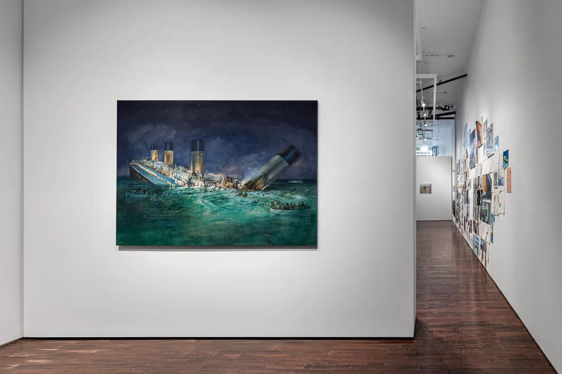 Gallery space with painting of a sinking ship in turquoise waters hung on white wall, wooden floor visible.