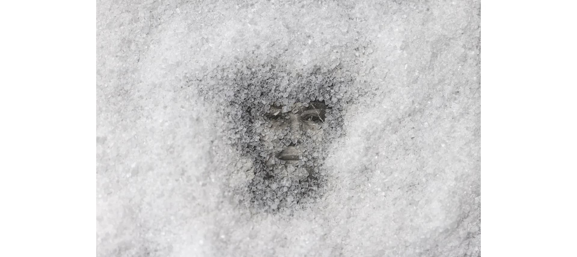 Grayscale portrait of a bearded man's face emerging from or dissolving into textured, speckled background in mixed-media technique.