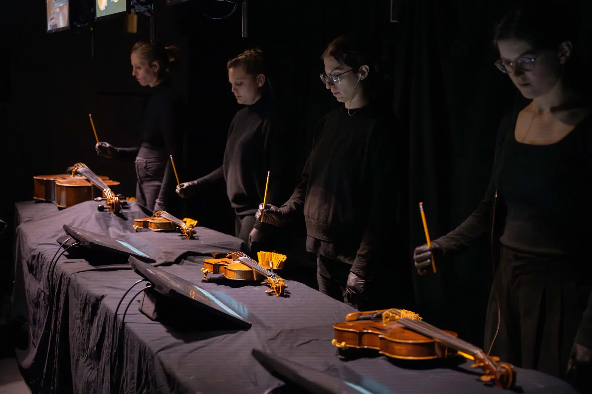 Culturehub performance or installation with four participants in black clothing arranged around golden/yellow string instruments on dark fabric under warm accent lighting.