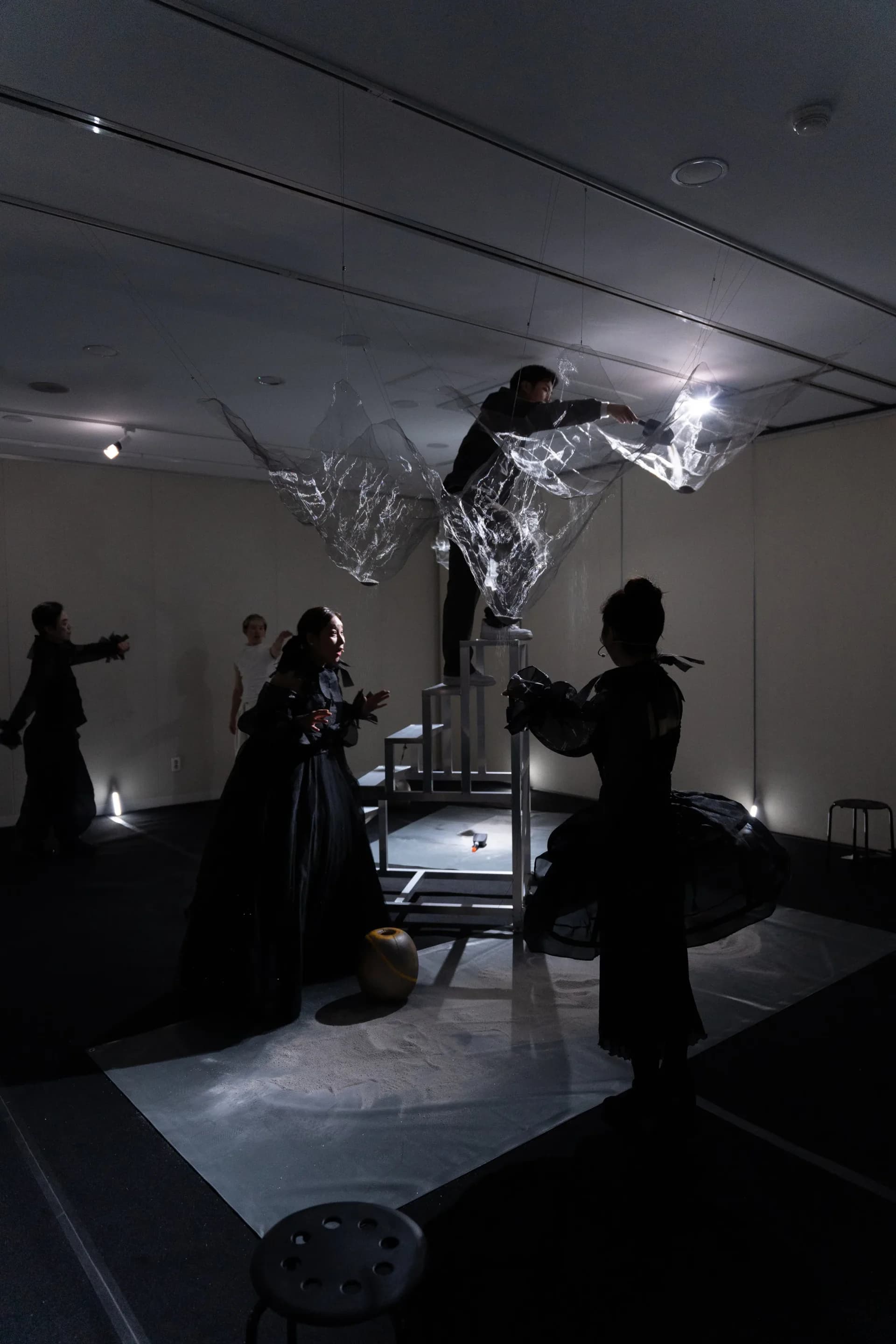 Culturehub immersive installation with silhouetted participants surrounding a suspended reflective sculptural figure illuminated from below in minimal light.