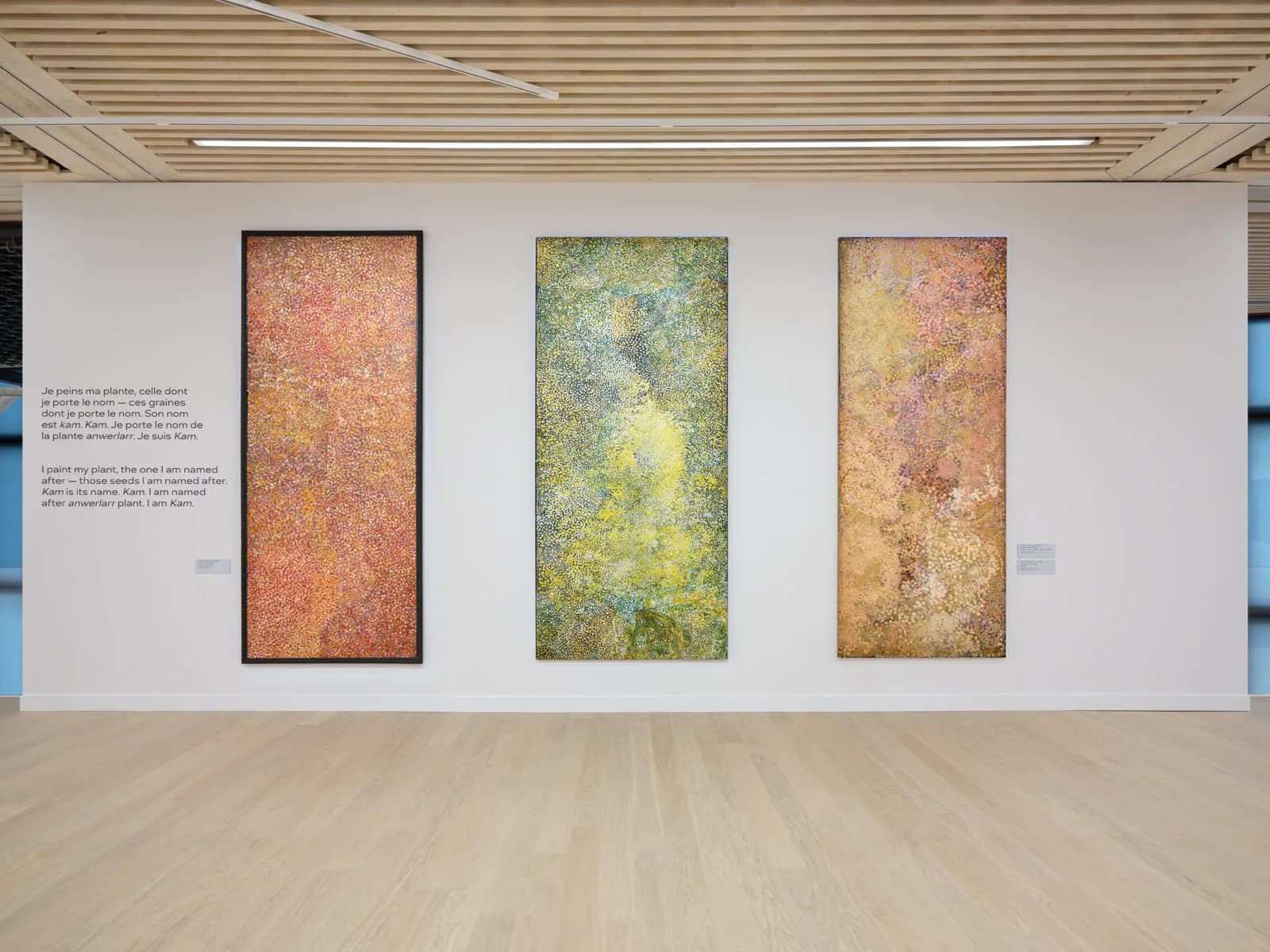 Gallery wall at D Lan Galleries displaying three tall vertical mixed-media artworks with textured surfaces in ochre, green, and rust tones.