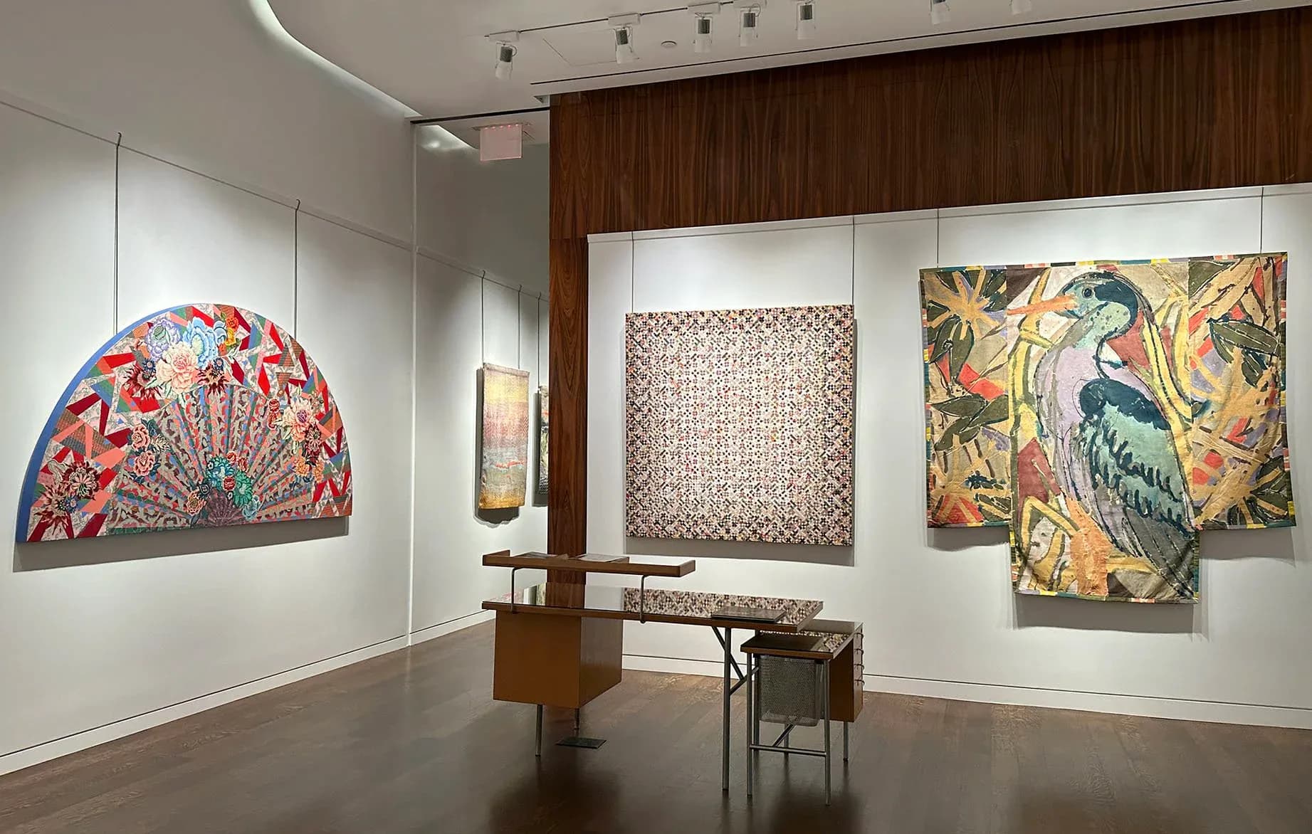 D. Wigmore Fine Art gallery wall with textile and mixed-media works including a red patterned dome-shaped piece, woven panel, and ornate bird painting.