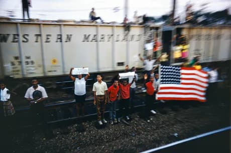 Color photograph of people standing in front of a Western Maryland railway car holding an American flag with motion blur effects.