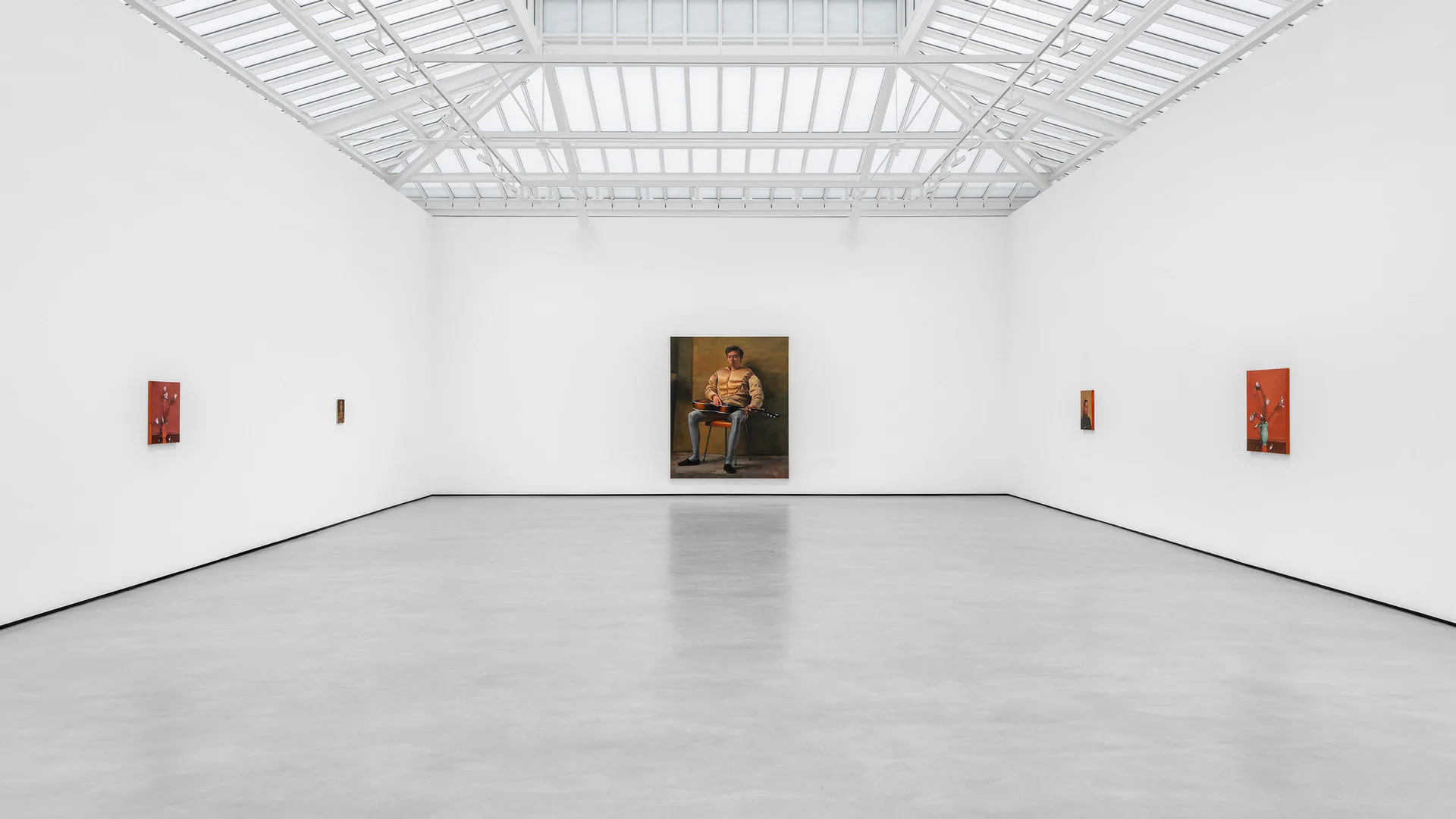 Minimalist gallery room with white walls, industrial grid ceiling, and polished floor. A dark figurative painting centered on far wall, with small red and orange artworks positioned symmetrically on left and right walls.