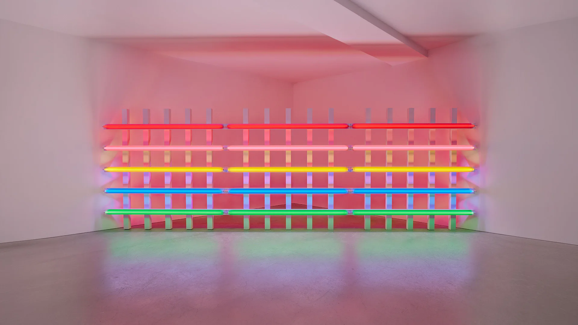 Neon light installation consisting of stacked horizontal fluorescent tubes in pink, yellow, blue, green, and purple, creating a layered rainbow effect with colorful reflection on floor.