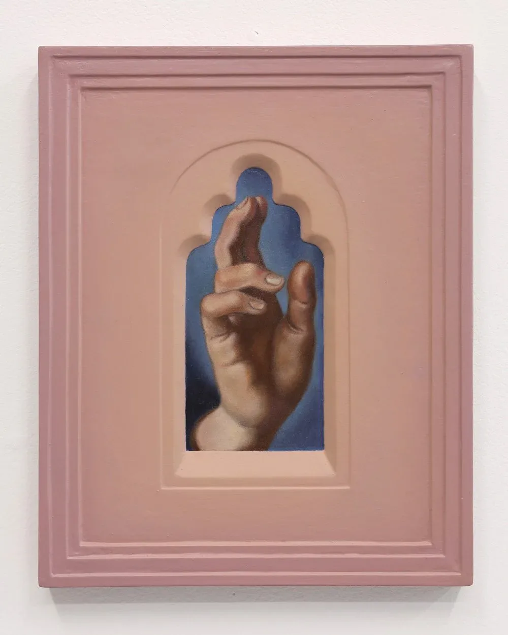 Framed sculptural relief in mauve-pink frame with molded white border featuring a naturalistic terracotta hand gesture against deep blue background.