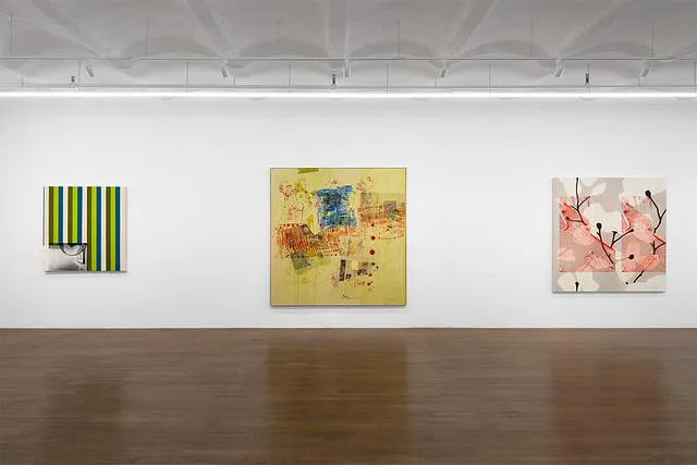 Gallery view with three artworks: striped green-yellow canvas left, yellow abstract composition center, pink floral work right.