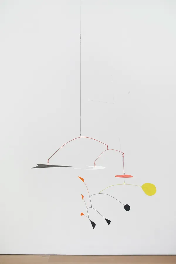 Kinetic mobile sculpture with red wire armatures, small geometric shapes in black, orange, and yellow, suspended from single line.