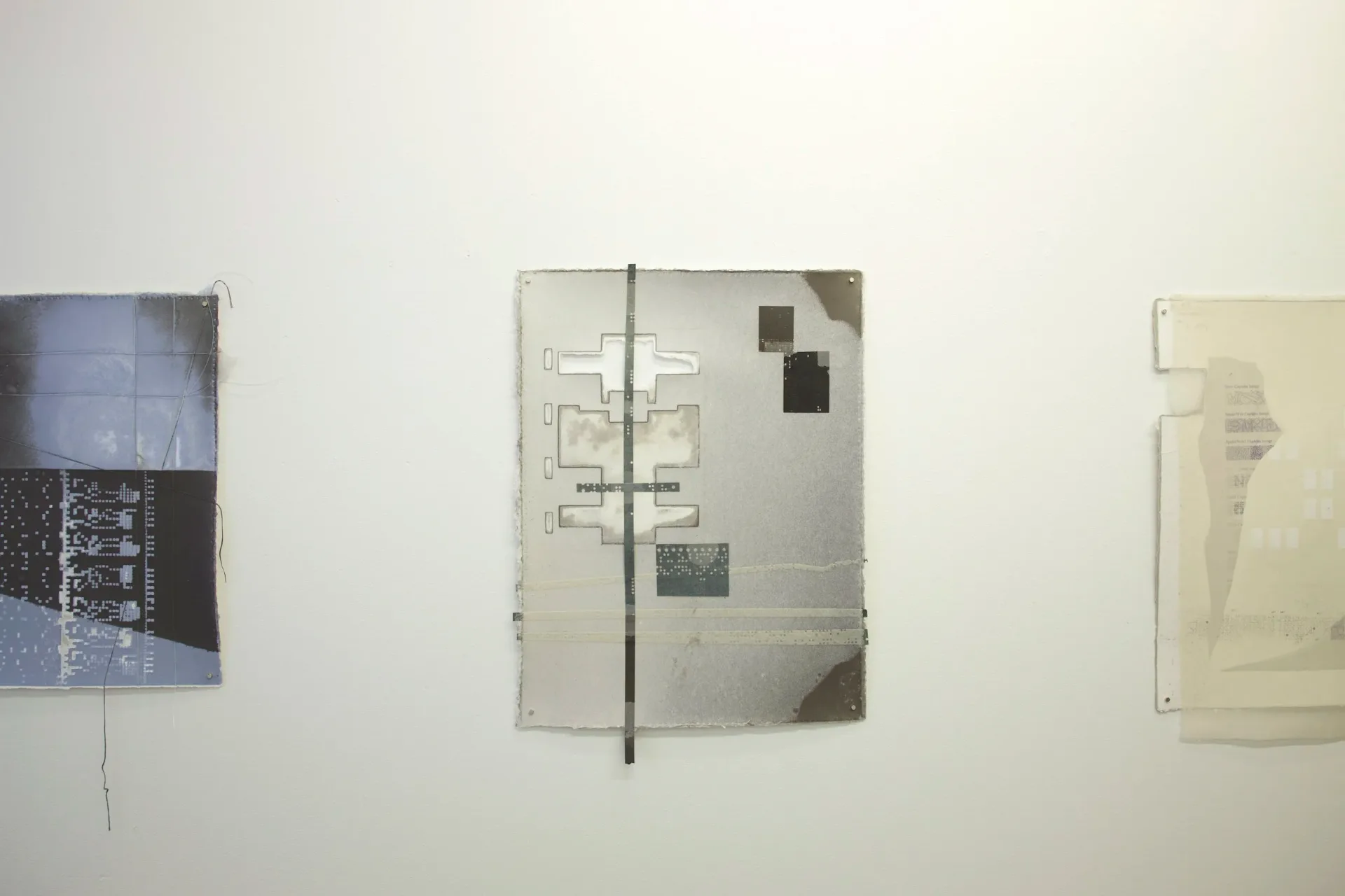Three translucent acrylic or resin panels mounted on wall with mixed-media compositions including architectural drawings, photographic elements, and layered materials.