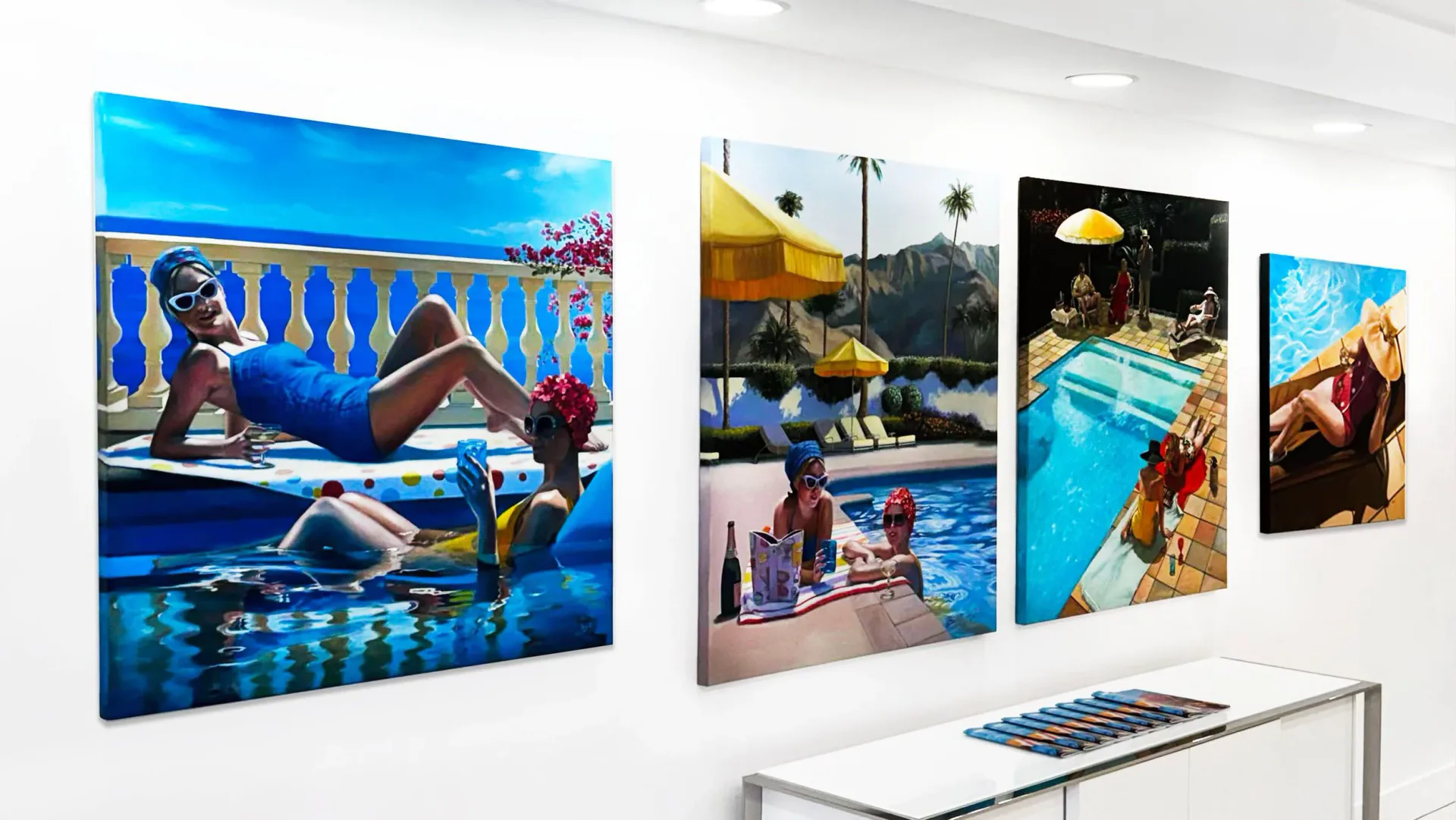Gallery interior showing four large colorful photographs mounted on white walls depicting swimmers and pool scenes in vibrant blues and warm tones.