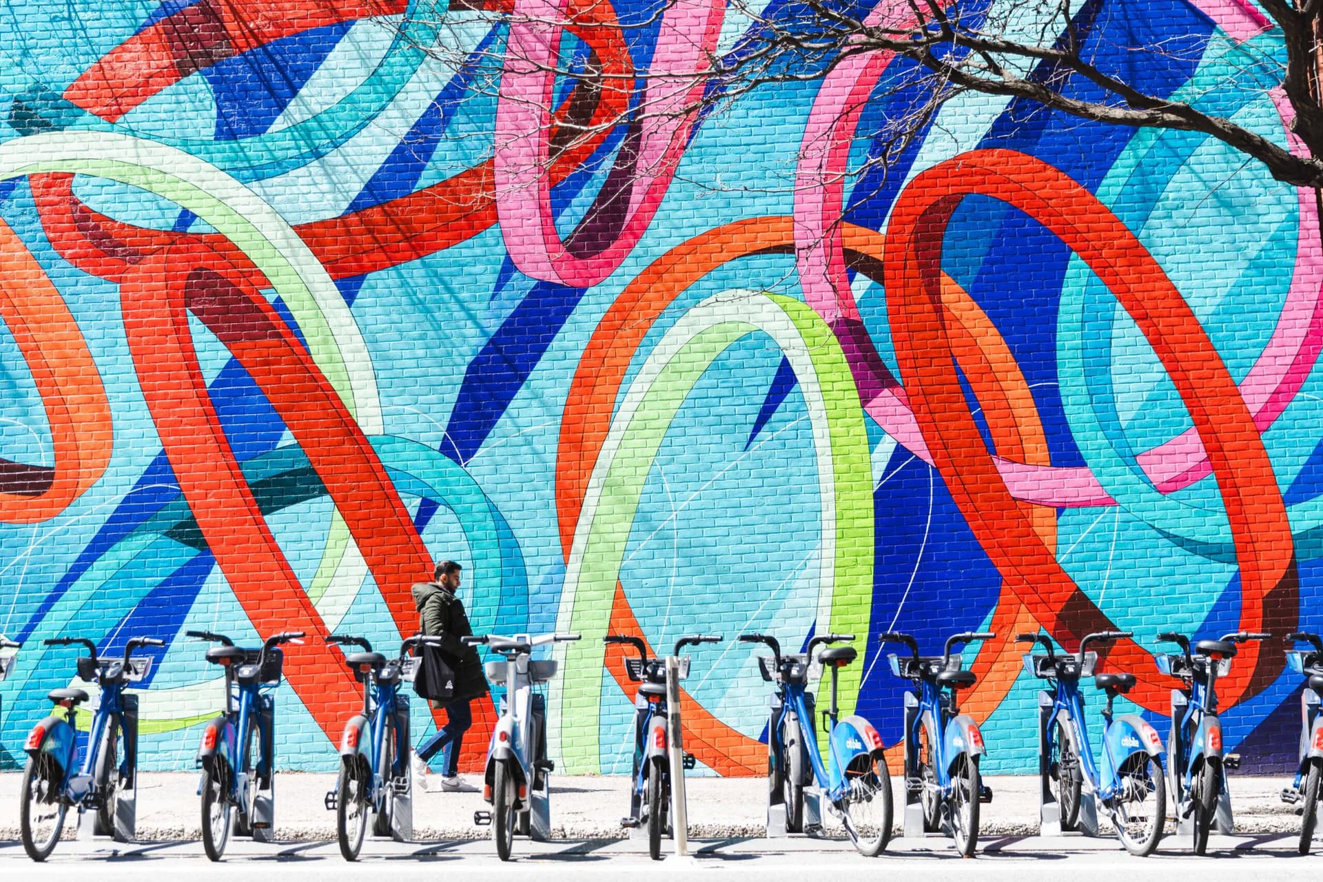 Vibrant mural with interlocking red, blue, and neon curves on brick wall; cyclists posed in front.