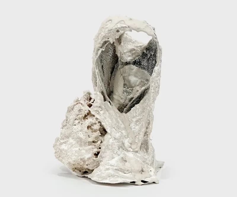 White plaster or ceramic sculpture with organic, hollowed forms suggesting an abstract face or head with textured surfaces.