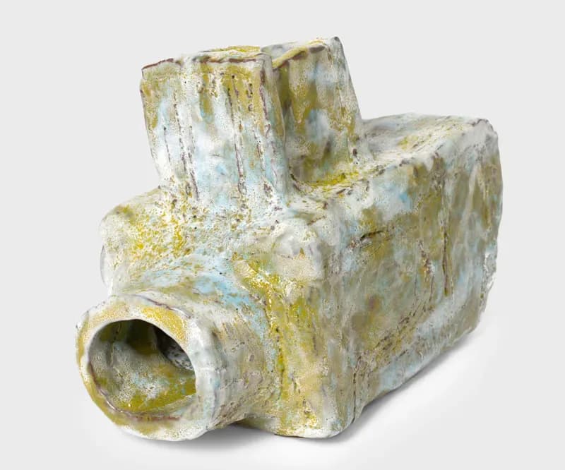 Sculptural ceramic or plaster form in white and yellow tones with angular, architectural shapes and a hollow tubular opening.