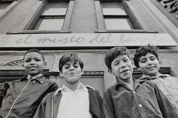 Black and white photograph of four young boys standing against an urban building facade with classical architecture details.