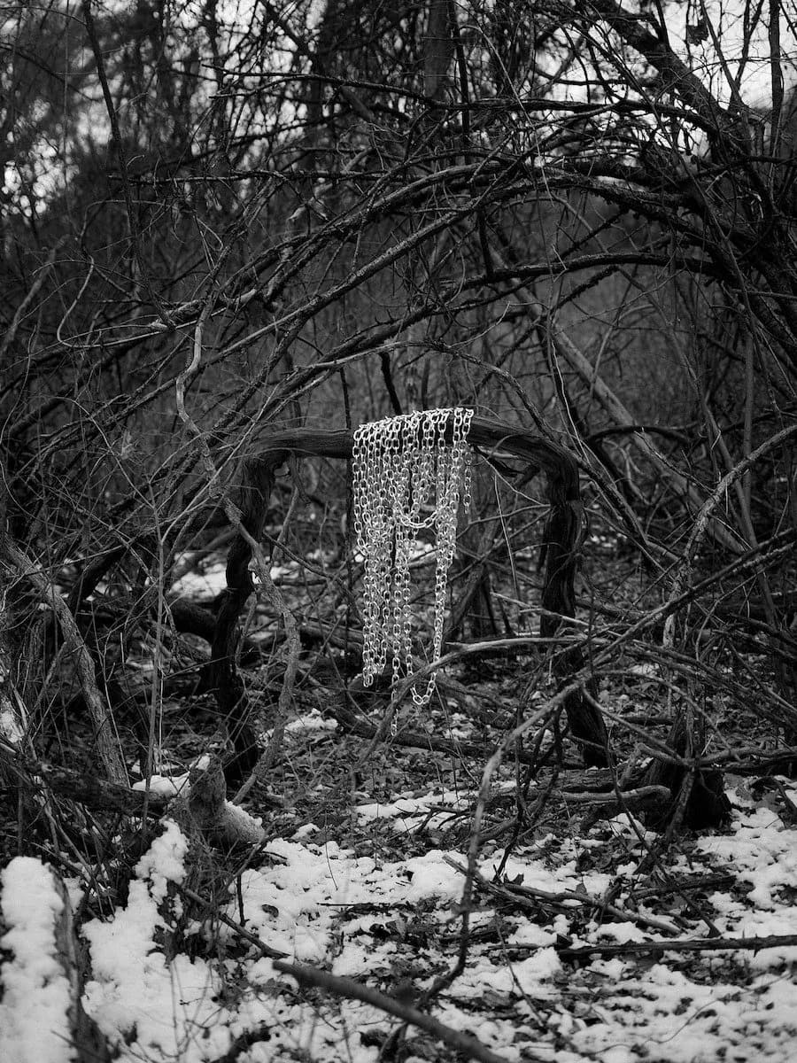 Black and white photograph of a tall textured cylindrical object surrounded by bare winter branches and snow.