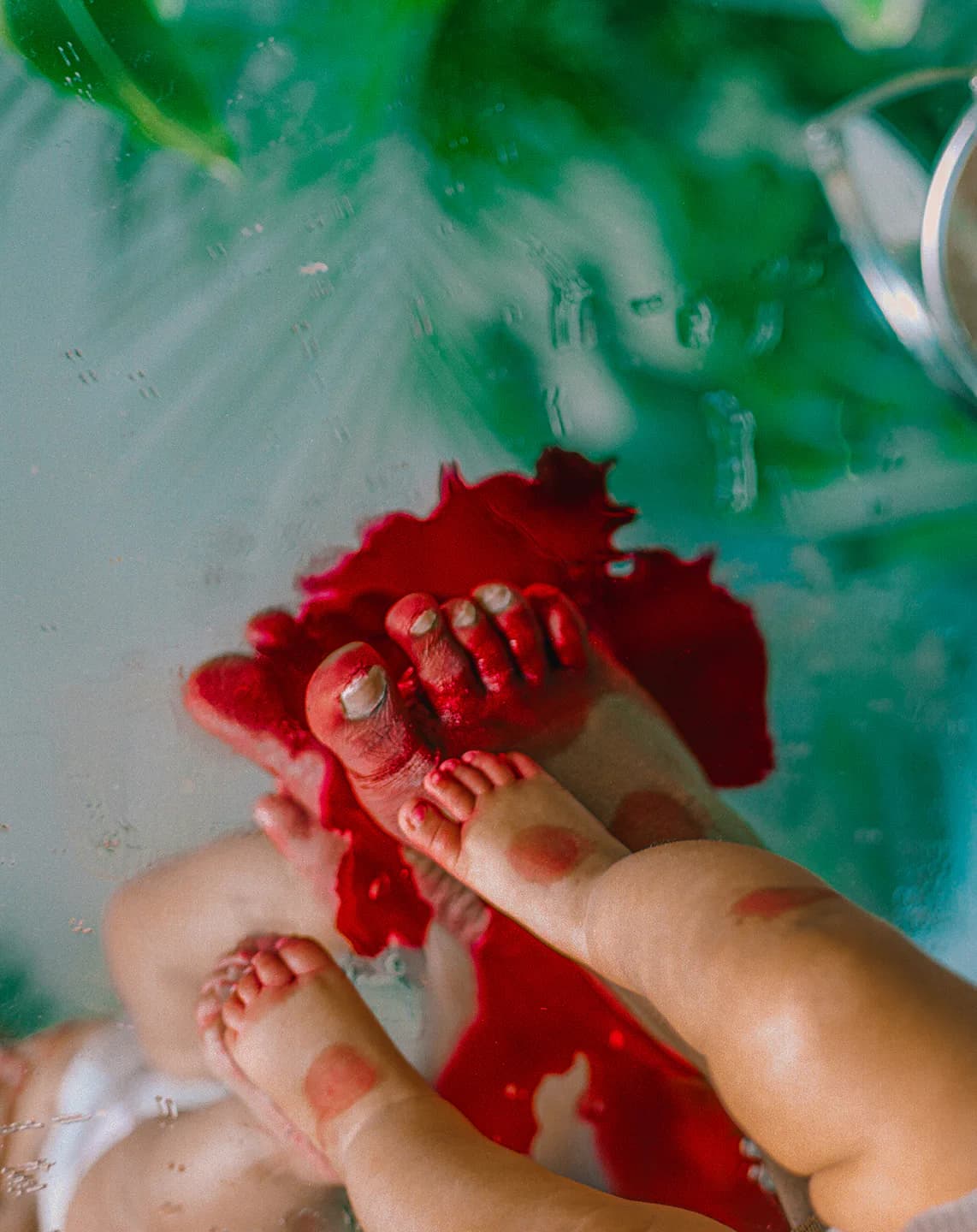 Child's hand creating red paint marks on green and white surface in an abstract, tactile composition.
