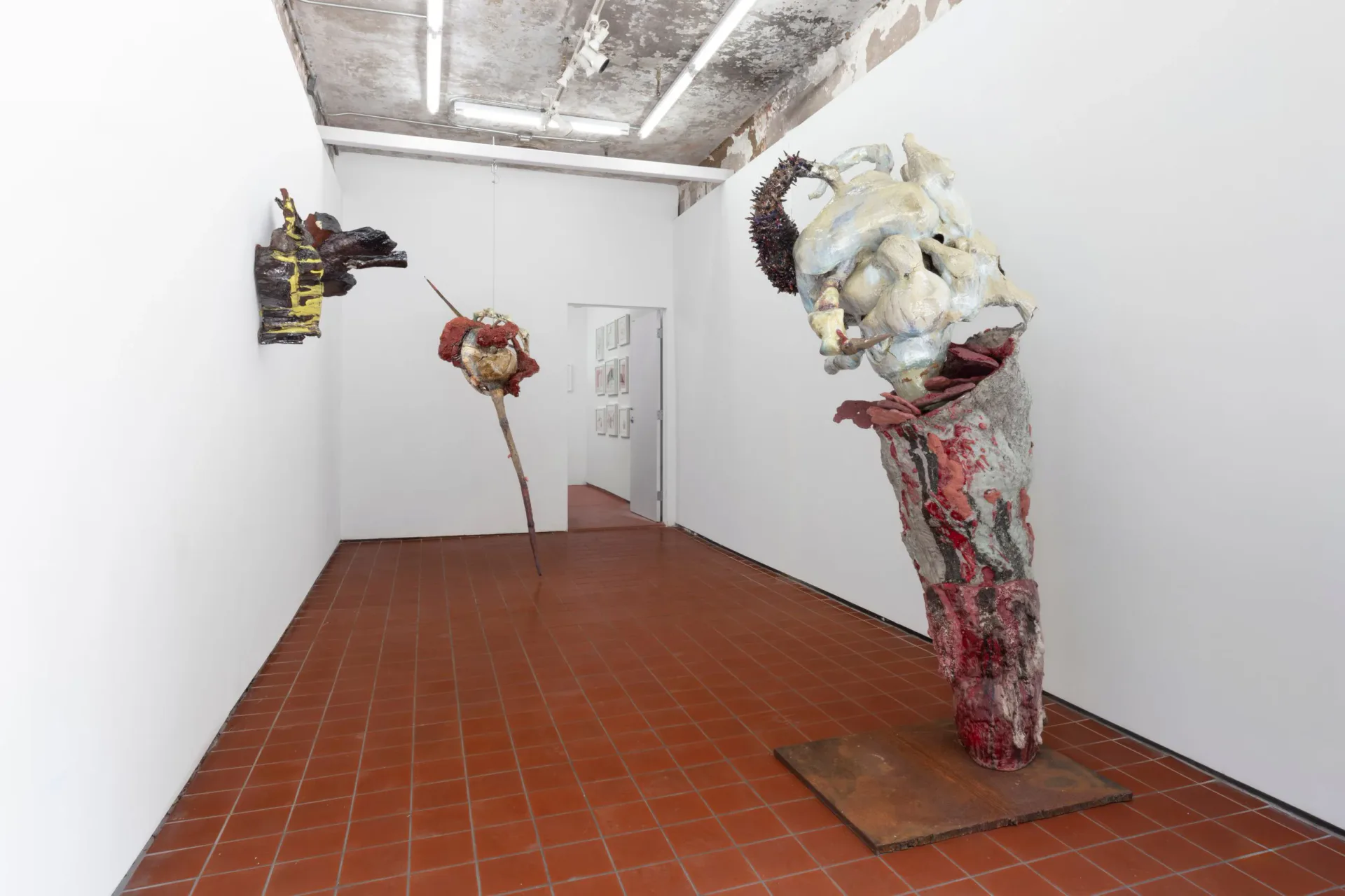 Gallery interior with terracotta tile floor, white walls, and sculptural installations including fabric-wrapped forms on pedestals.