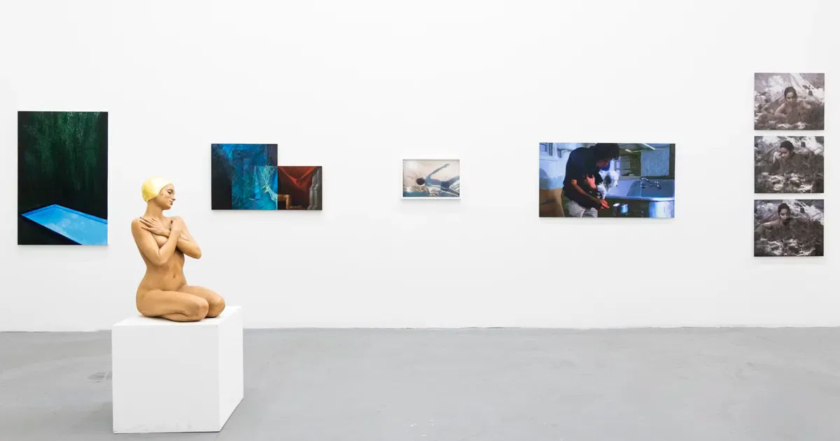 Gallery interior at Ethan Cohen Gallery with white walls, pedestal displaying wooden kneeling figure sculpture, and mixed-media works including photographs and video projections.