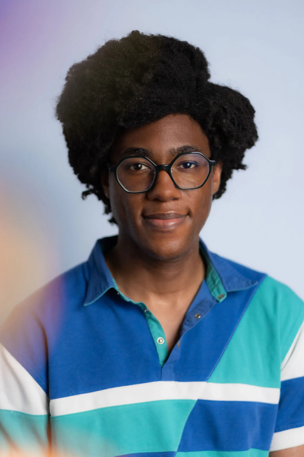 Person with dark textured hair wearing clear-framed glasses and a colorblocked blue and turquoise shirt with white stripe.