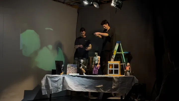 FiveMyles gallery interior with two people standing on a stage beside a table displaying art objects and books under spotlights.