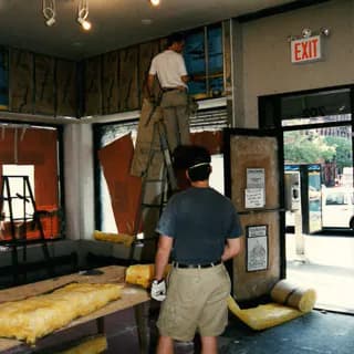 Two people examining large sculptural materials and installations inside Fountain House Gallery, with EXIT sign and storefront visible.