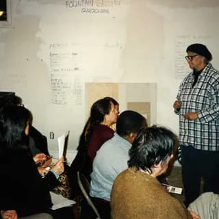 Group of visitors gathered around wall display and presentation at Fountain House Gallery during event.