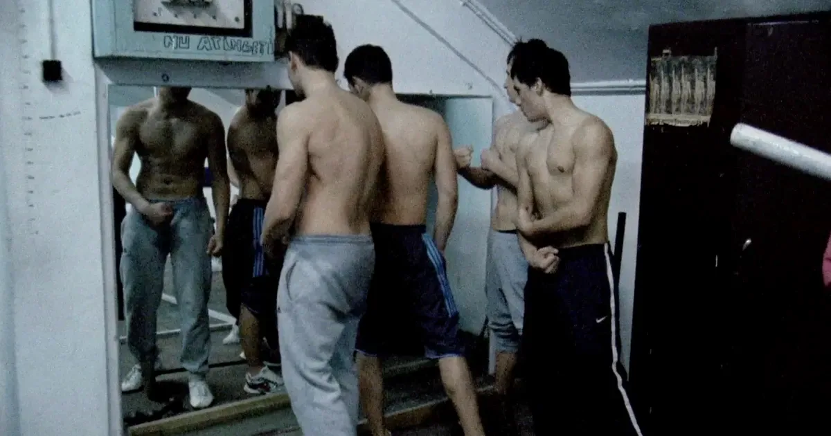 Four shirtless male figures viewed from behind in an institutional room with mirrors and white walls, mixed-media artwork exploring bodily presence and reflection.