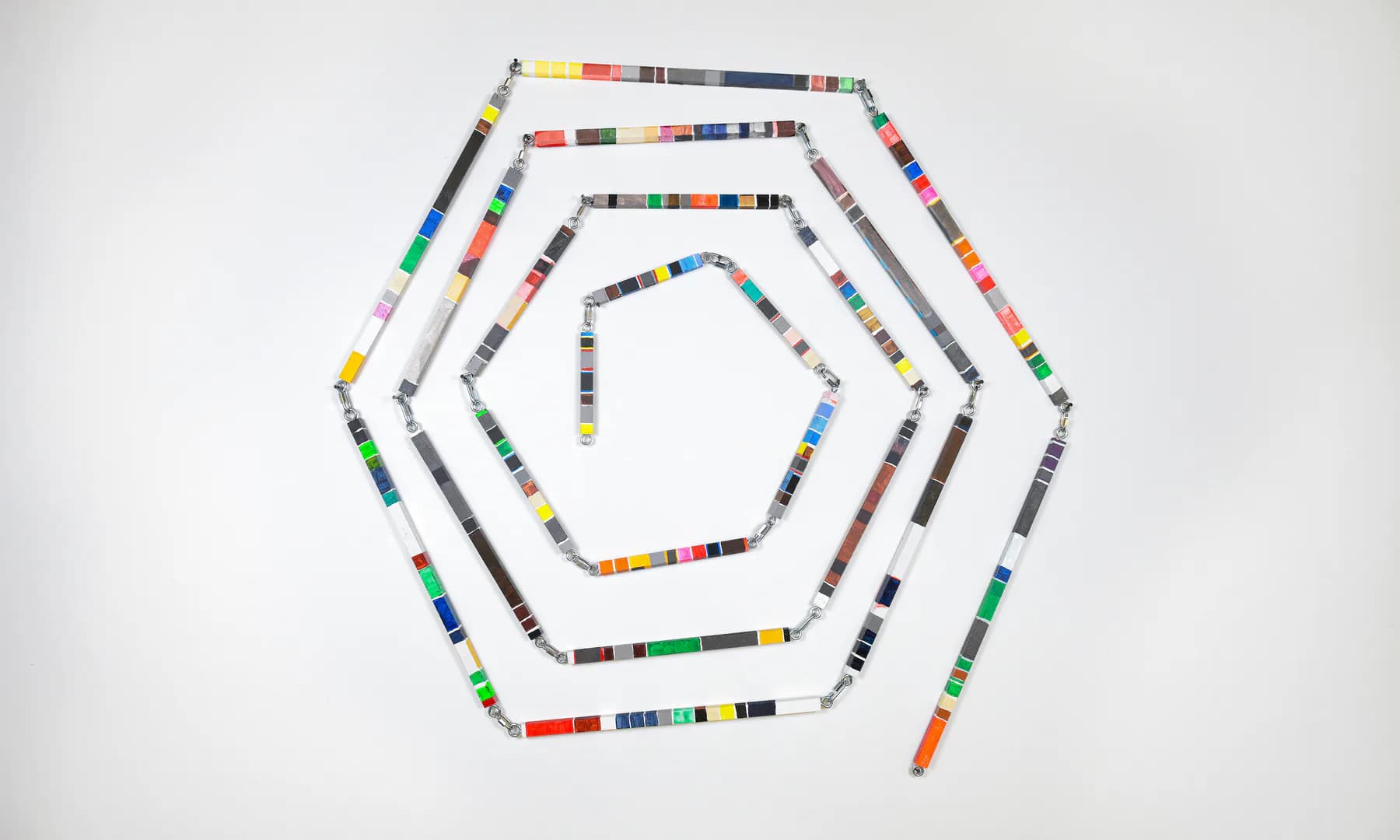 Concentric hexagons made from colorful segmented beads or blocks arranged in nested geometric patterns against a white background.