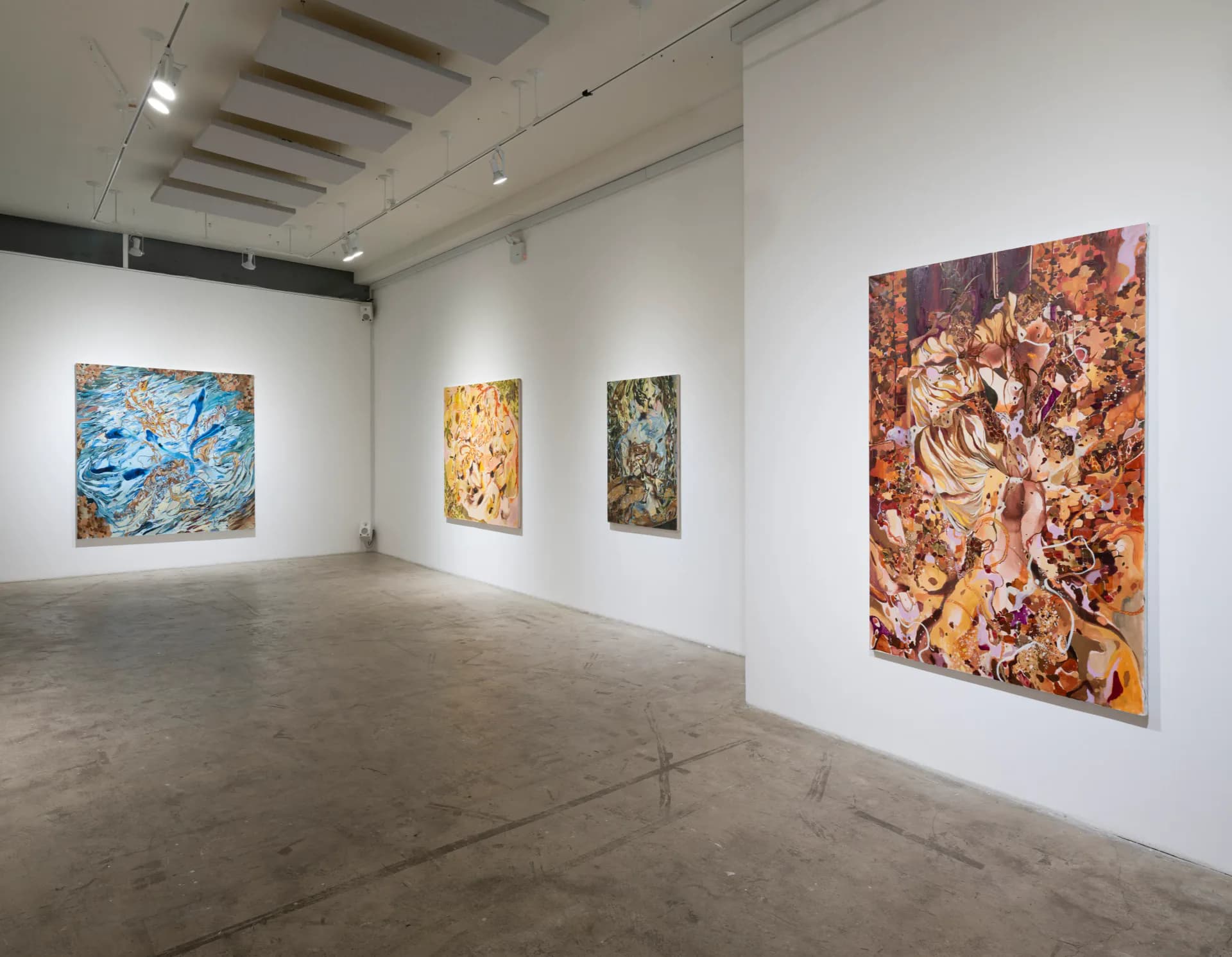 Gallery space with recessed ceiling lights and four abstract paintings in varied colors—blue, gold, olive, and coral—mounted on white walls.