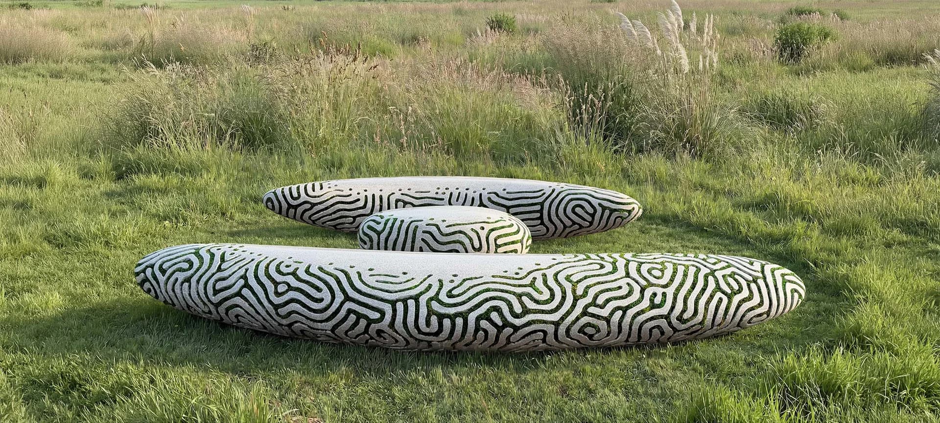 Two stacked sculptural forms with black and white striped patterns resembling zebra stripes, placed on grass outdoors.