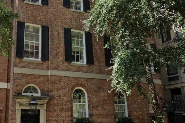 Photograph of historic brick townhouse facade with ivy vines, arched windows, black shutters, and classical stone details.