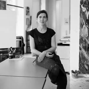 Black and white photograph of a woman in black sleeveless shirt seated in minimalist studio interior.