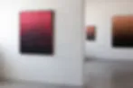 Gallery interior showing abstract paintings with pink-to-black gradients and warm tones on white walls.