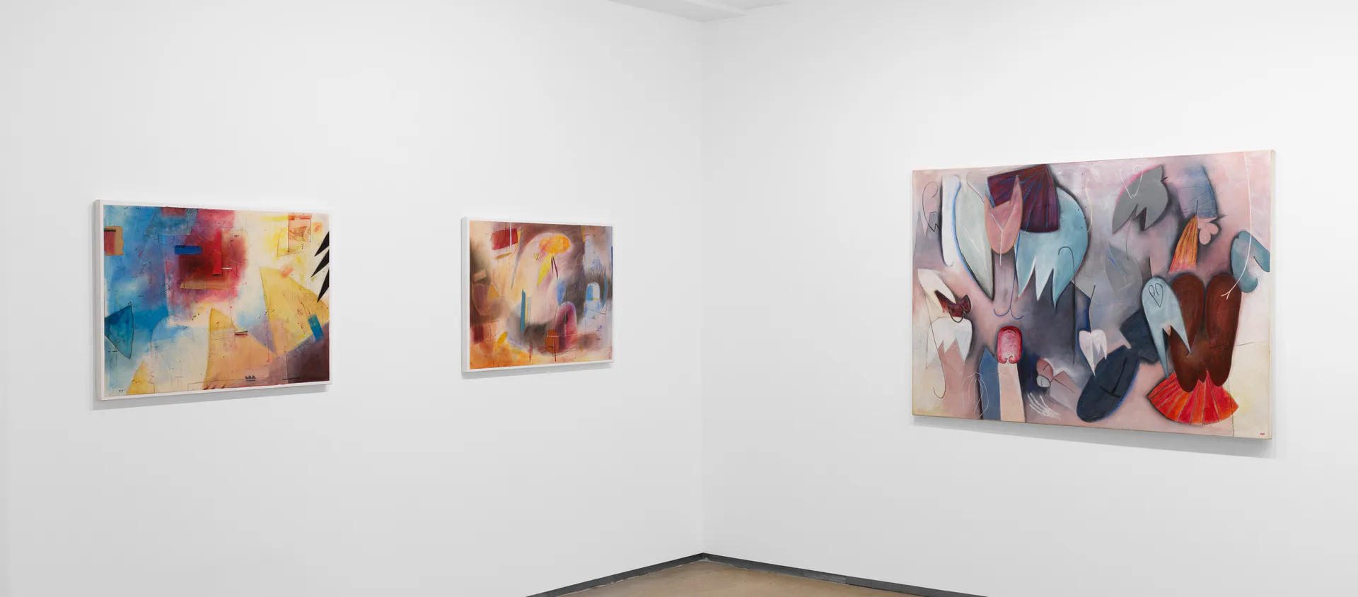 White gallery interior with three abstract paintings in warm and cool tones displayed on walls.