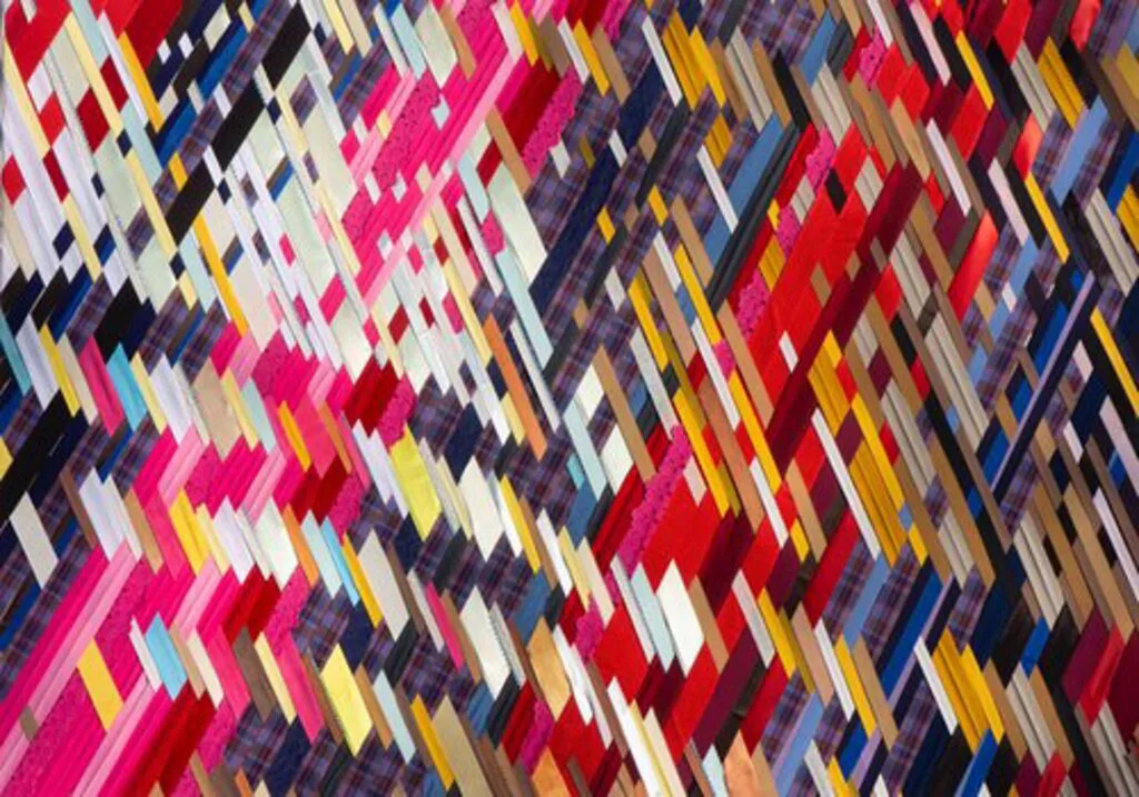 Abstract textile or woven artwork featuring a dense chevron pattern in vibrant multicolors including hot pink, navy, white, and gold.