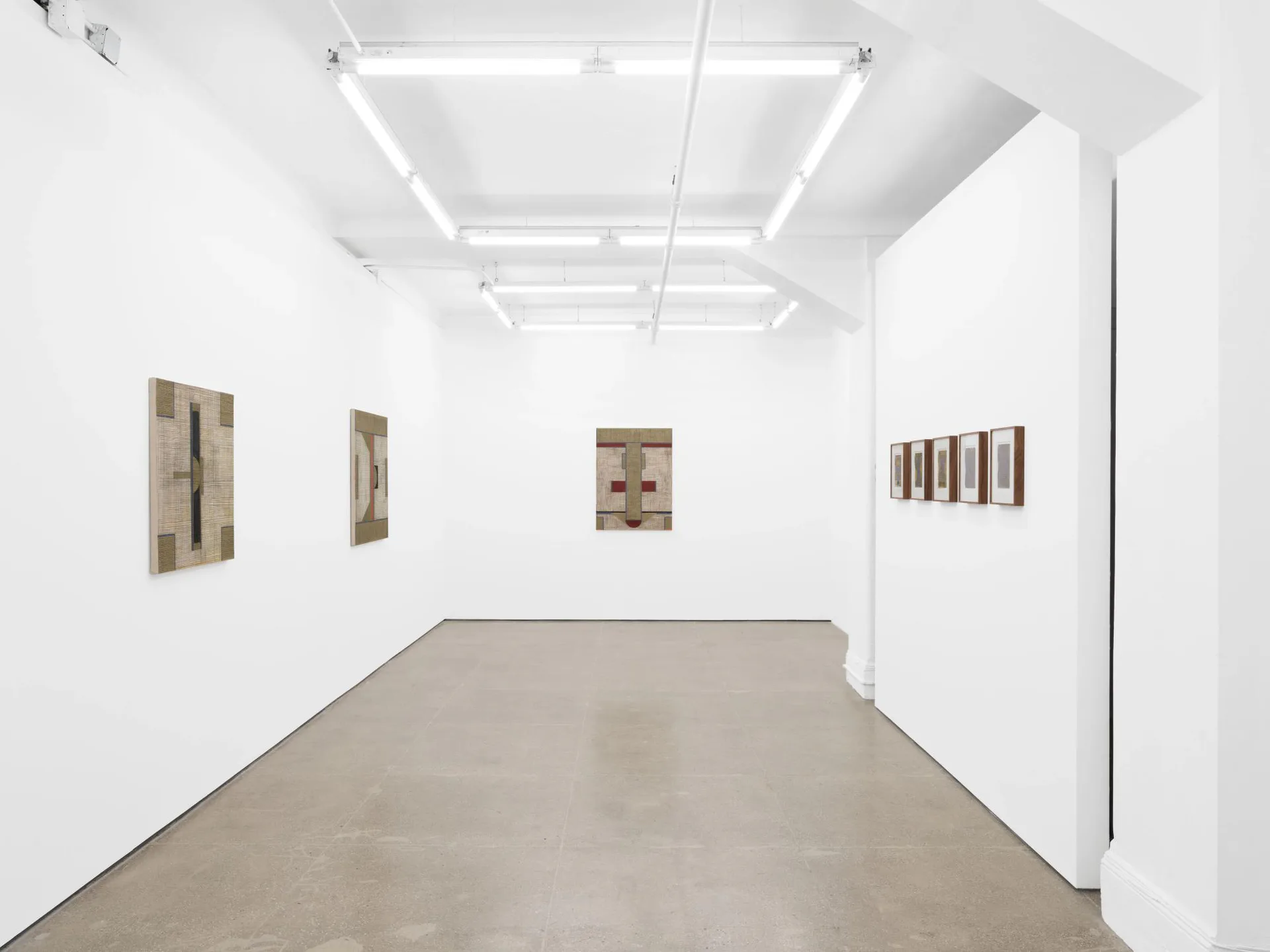 Bright white gallery interior with fluorescent ceiling lights and four framed artworks displayed on white walls at Gordon Robichaux.