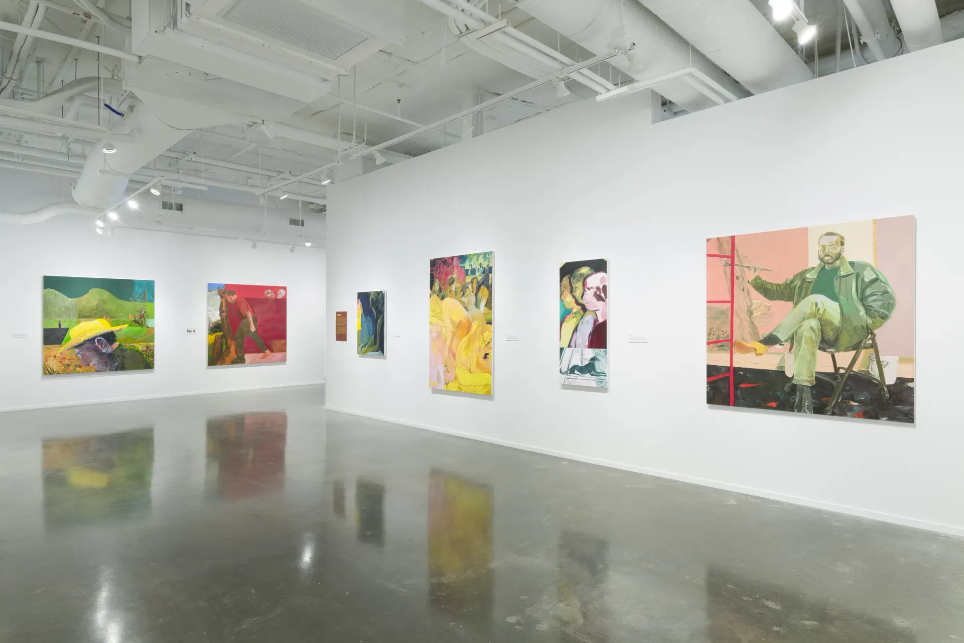 Modern gallery with polished concrete floors, industrial ceiling, and white walls displaying varied colorful paintings and mixed-media works of different sizes.